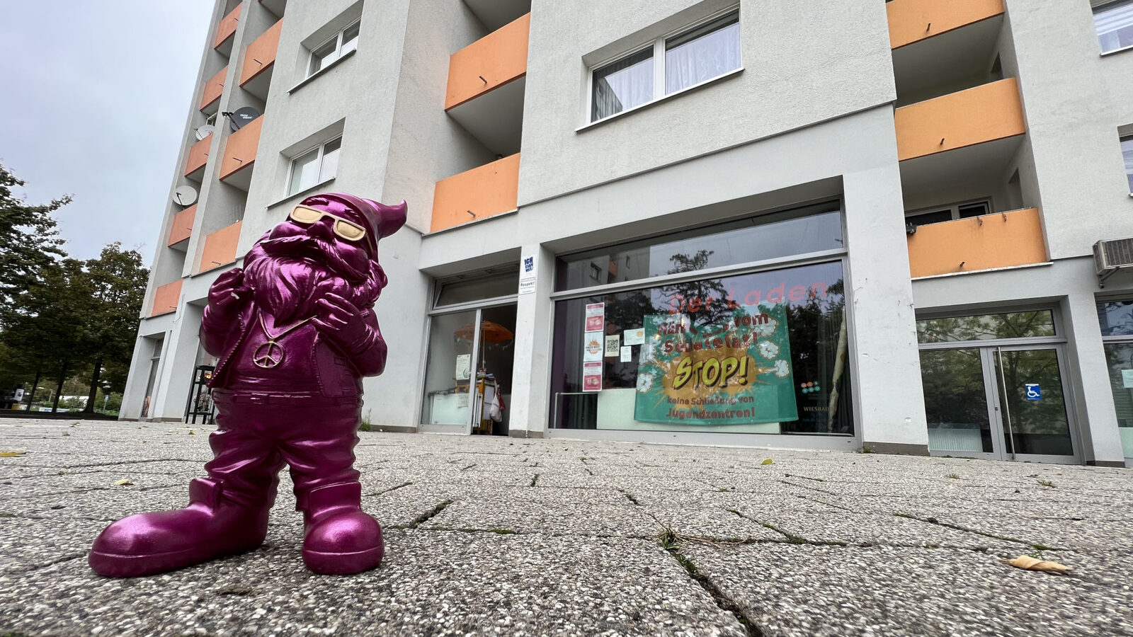 A pink garden gnome stands on exposed aggregate concrete slabs in front of a store front.