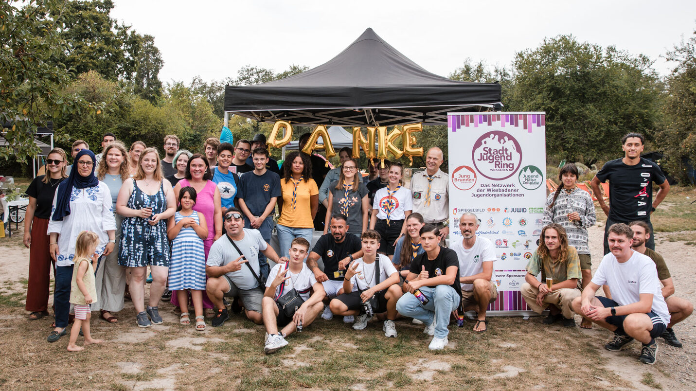 Eine große Gruppe von Menschen steht vor Ballons, die ein "Danke" formen und vor dem Rollup des Stadtjugendrings.