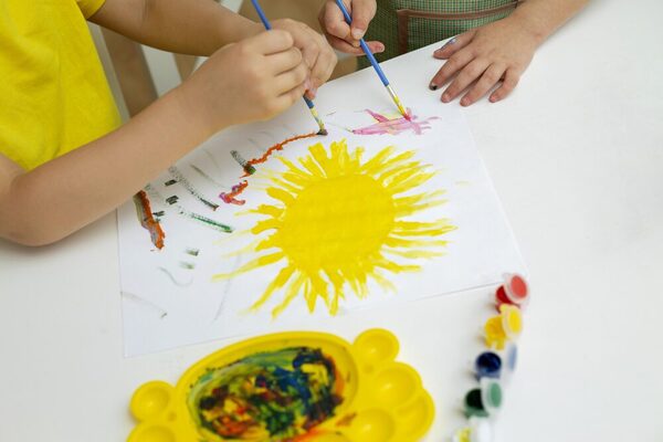 Kinder malen eine Sonne mit Wasserfarben.