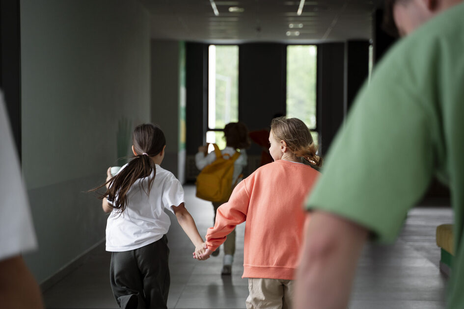 Zwei Kinder rennen Hand in Hand im Schulflur.