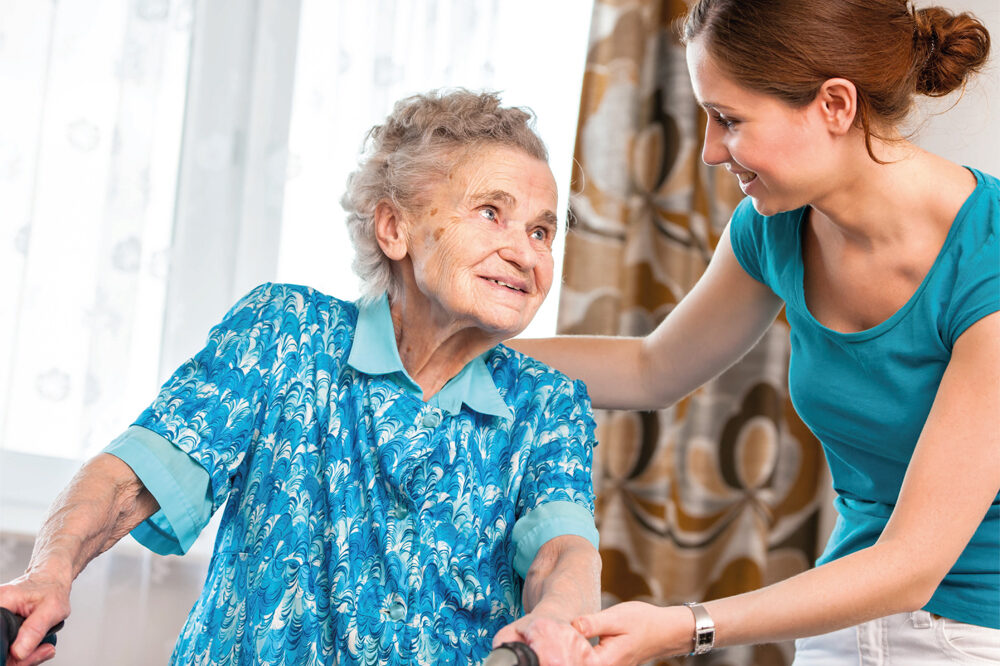 Ältere Frau mit Gehhilfe und Pflegerin