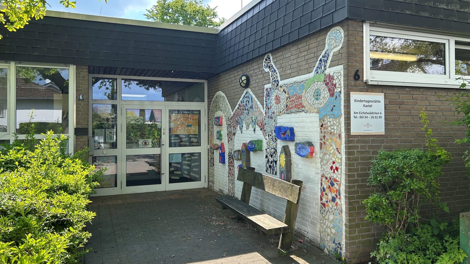 Der Eingang der Kindertagesstätte - an der rechten Wand ist ein Mosaik, davor steht eine Bank
