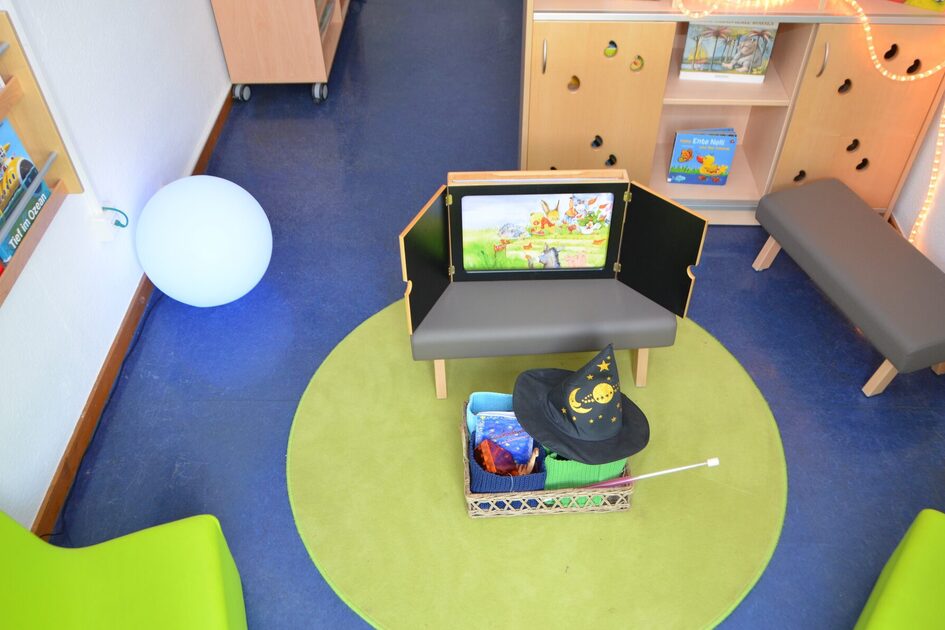 Der Leseraum der Kindertagesstätte. In der Mitte ein Tisch mit einem Kamishibai - ein Erzähltheater mit großen Bildkarten