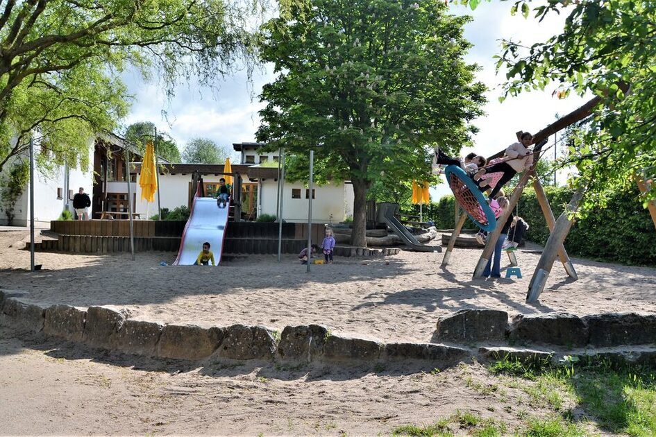 Das Außengelände der Kindertagesstätte mit einem großen Sandspielbereich, einer Schaukel und einer Rutsche