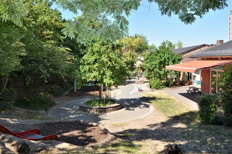 The outdoor area of the daycare center with a slide on the slope. The daycare center building is on the right-hand side