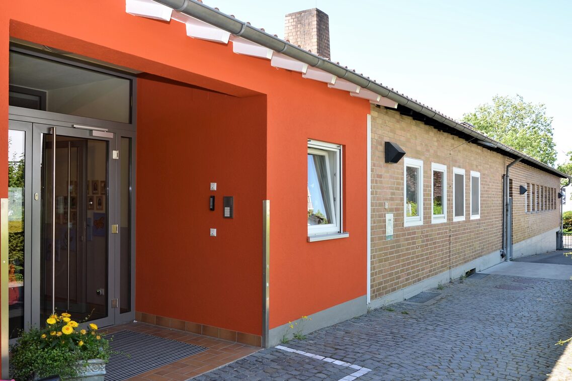 The building of the daycare center with a red entrance area. Flowers in a tub in front of the door