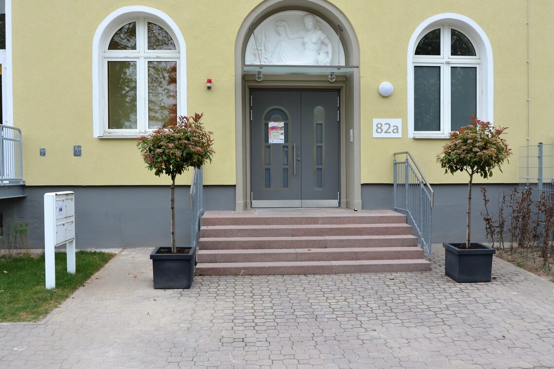 Der Eingangsbereich der Kindertagesstätte. Links und rechts neben der Treppe stehen kleine Bäume im Topf