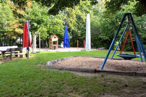 Das Außengelände der Kindertagesstätte mit einer Nestschaukel, Sitzgelegenheiten und dem Sandspielbereich