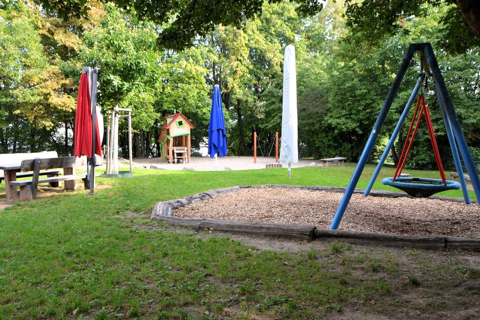 Das Außengelände der Kindertagesstätte mit einer Nestschaukel, Sitzgelegenheiten und dem Sandspielbereich