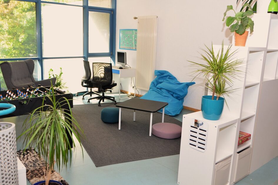 Der Clubraum der Kindertagesstätte mit gemütlichen Sitzelementen, Pflanzen, einem Computerarbeitsplatz und einem Tischkicker