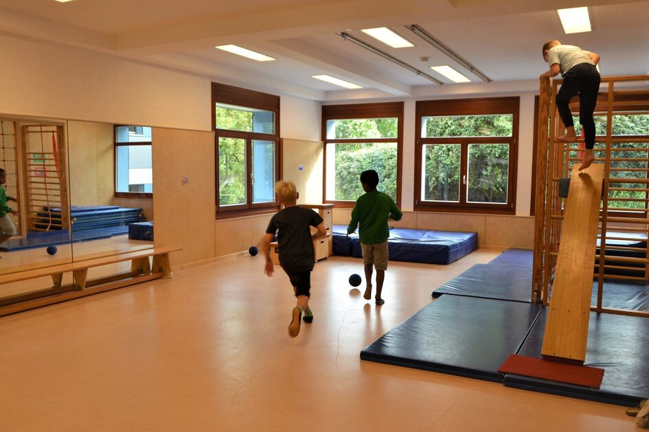 Der Bewegungsraum der Kindertagesstätte. Links hängt ein großer Spiegel und auf der rechten Seite steht ein Kletterelement. Auf dem Boden liegen blaue Matten