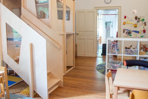 Hier sehen Sie die Treppe zur zweiten Ebene in einem Gruppenraum. An der rechten Wand steht ein Tisch mit Stühlen