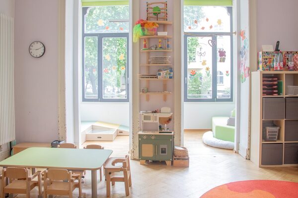 Ein Gruppenraum in der Krippe. Im Vordergrund steht ein kleiner Tisch mit Stühlen. An der hinteren Wand der Durchgang zu einem Erker