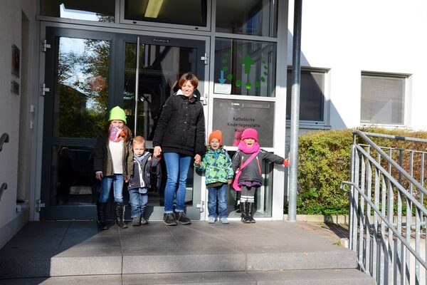 يمكنك رؤية مدخل مركز الرعاية النهارية. امرأة تحمل أطفالها بيدها وتقف أمام الباب