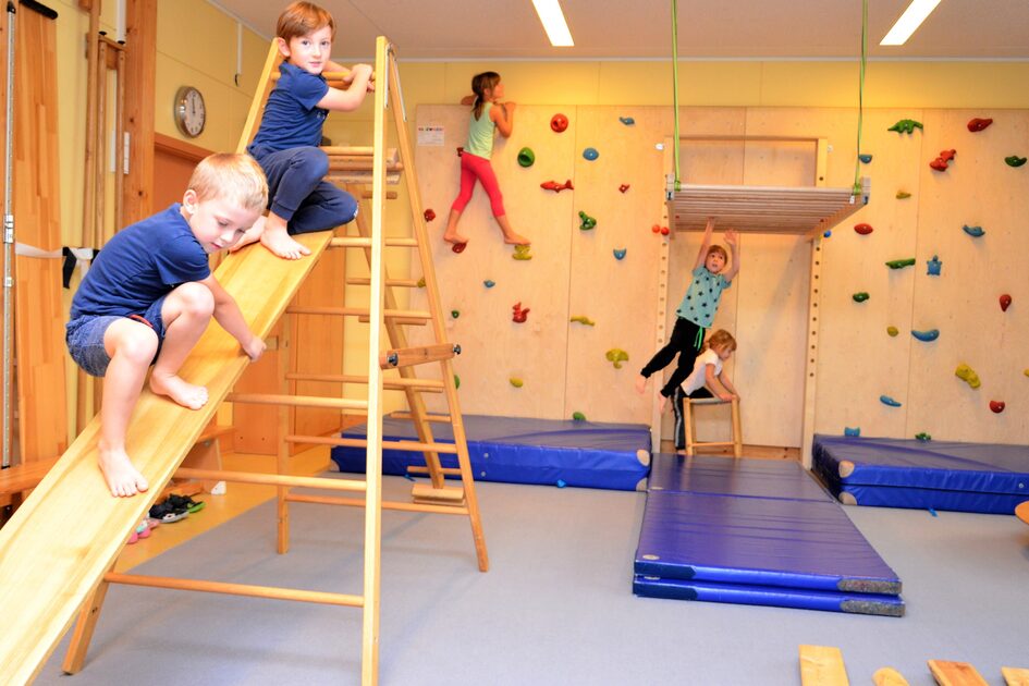 Der Bewegungsraum der Kindertagesstätte mit einer Kletterwand und einer Kletterleiter mit Rutsche.