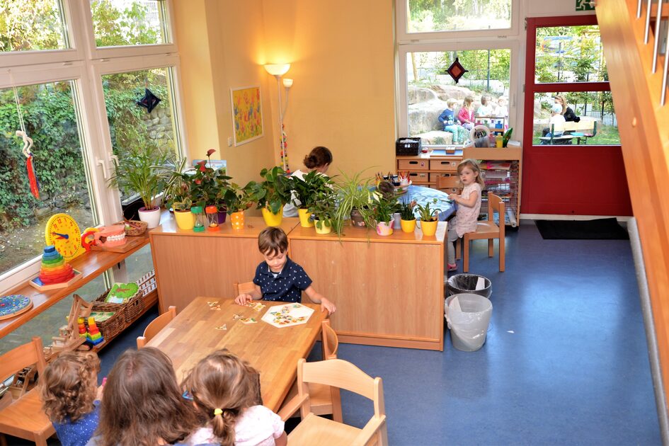 Ein Gruppenraum im Elementarbereich. An den Tischen spielen Kinder. Auf dem Regal stehen verschiedene Pflanzen.