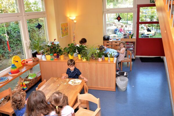 Ein Gruppenraum im Elementarbereich. An den Tischen spielen Kinder. Auf dem Regal stehen verschiedene Pflanzen.