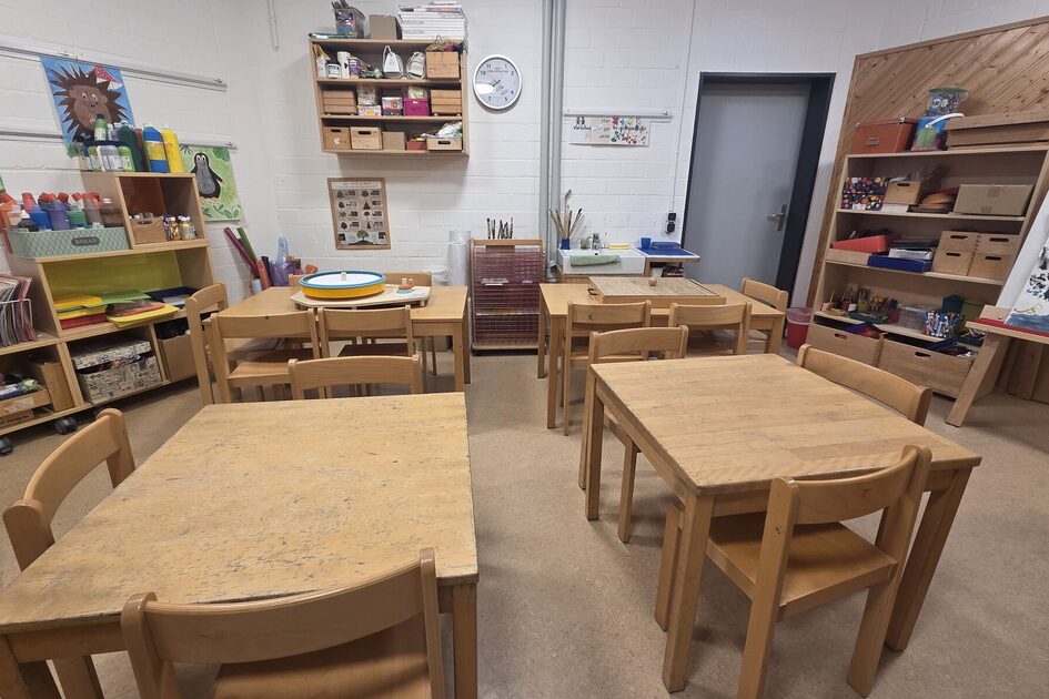 The creative workshop with four large work tables and chairs. Shelves on the walls with materials for crafting and painting.