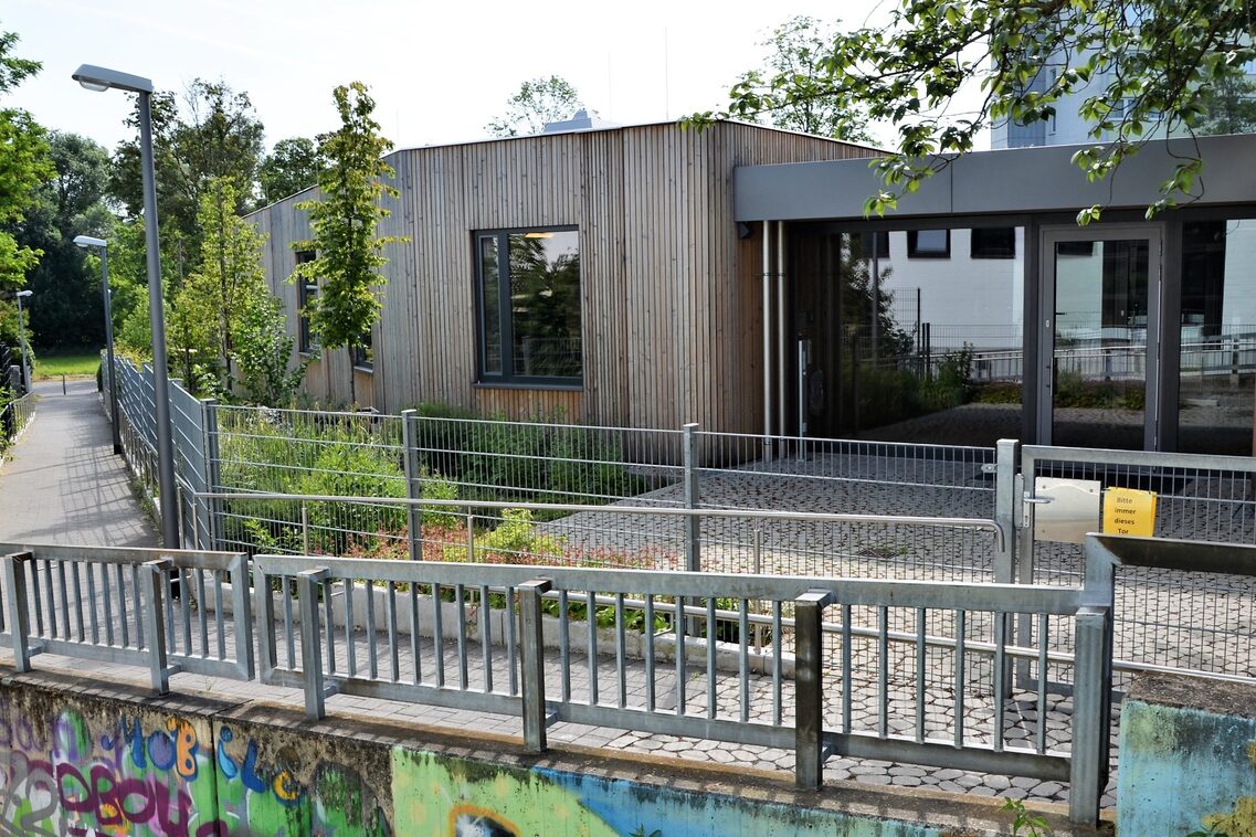 The entrance area of the daycare center is easily accessible via stairs and a ramp. The building is surrounded by trees and plants