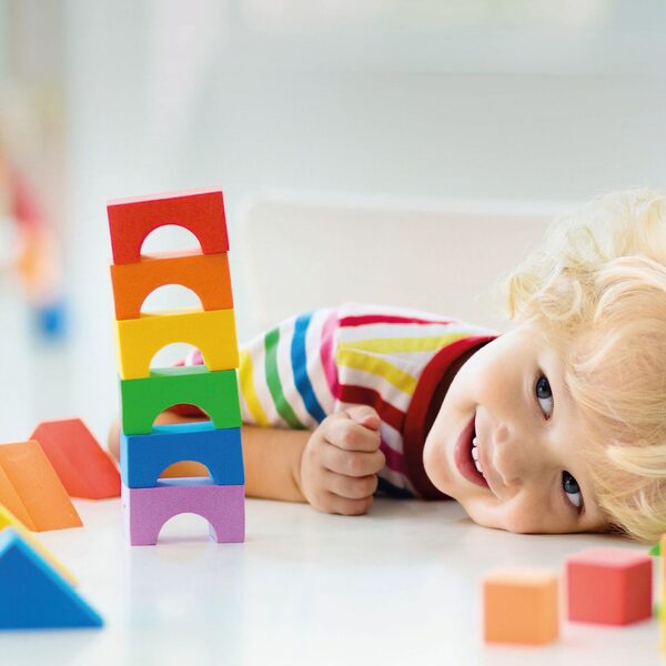 Ein Kind, die Wange auf dem Tisch liegend, davor übereinander gestapelte bunte Bauklötze.