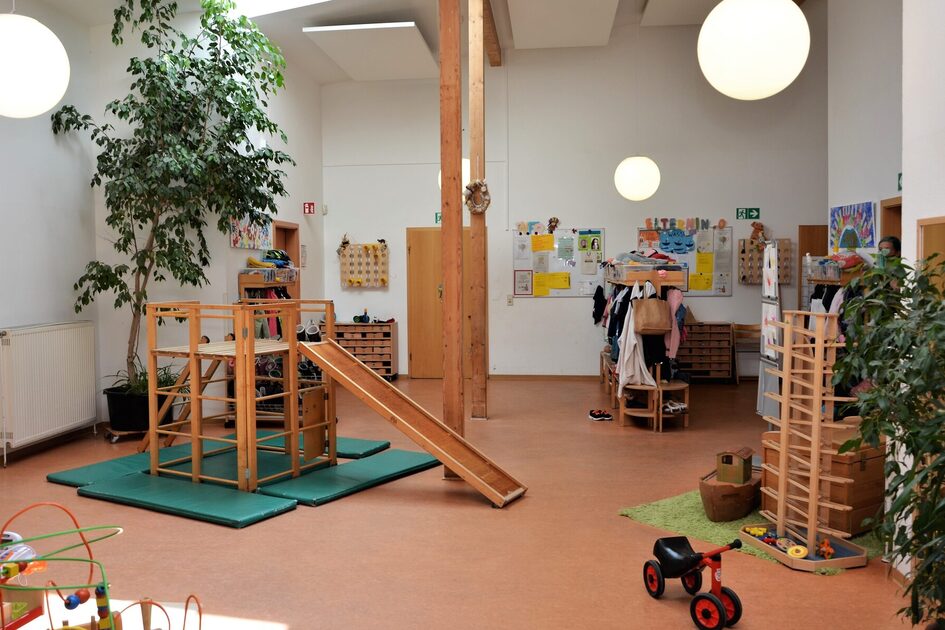 Der Flur der Kindertagesstätte. In der Mitte steht ein Klettergerüst mit einer Rutsche. An der rechten Seite ist eine große Murmelbahn