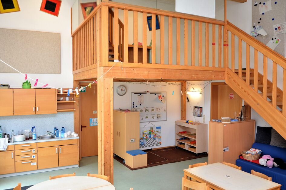 Der Grupperaum mit einer zweiten Ebene. Auf der linken Seite ist eine Küchenzeile. Unter der Ebene ist ein Teppich mit Spielmaterial