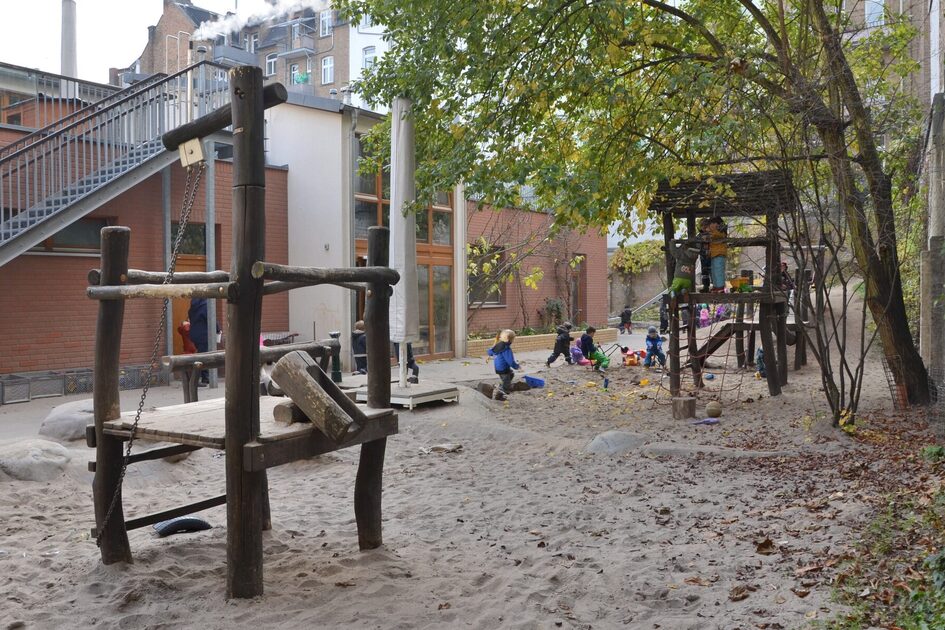 Das Außengelände mit einem Kletterhaus in einem großen Sandspielbereich. Links ist das Gebäude der Kindertagesstätte