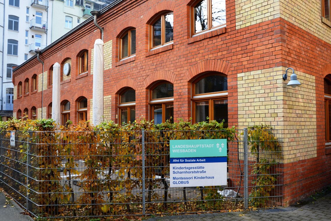 Die Kindertagesstätte ist in einem alten Backsteingebäude mit Rundbogenfenster. Vor den Gruppen ist ein kleiner Vorgarten.