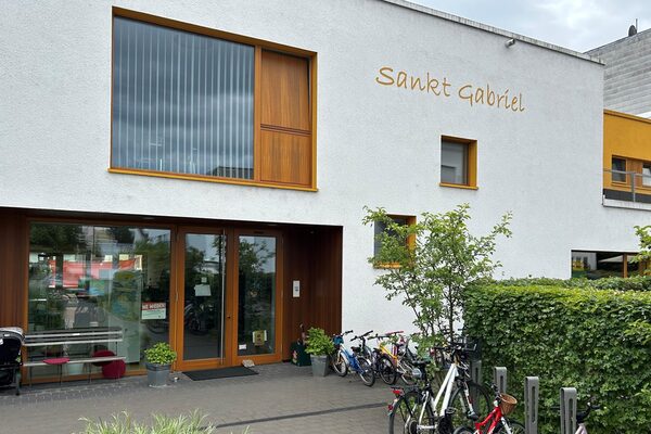 Der Eingangsbereich der Kindertagesstätte. Rechts ist ein Fahrradständer mit Rädern. Der Schriftzug St. Gabriel steht an der Hauswand