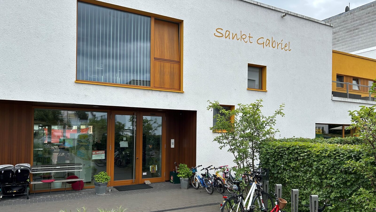 Der Eingangsbereich der Kindertagesstätte. Rechts ist ein Fahrradständer mit Rädern. Der Schriftzug St. Gabriel steht an der Hauswand