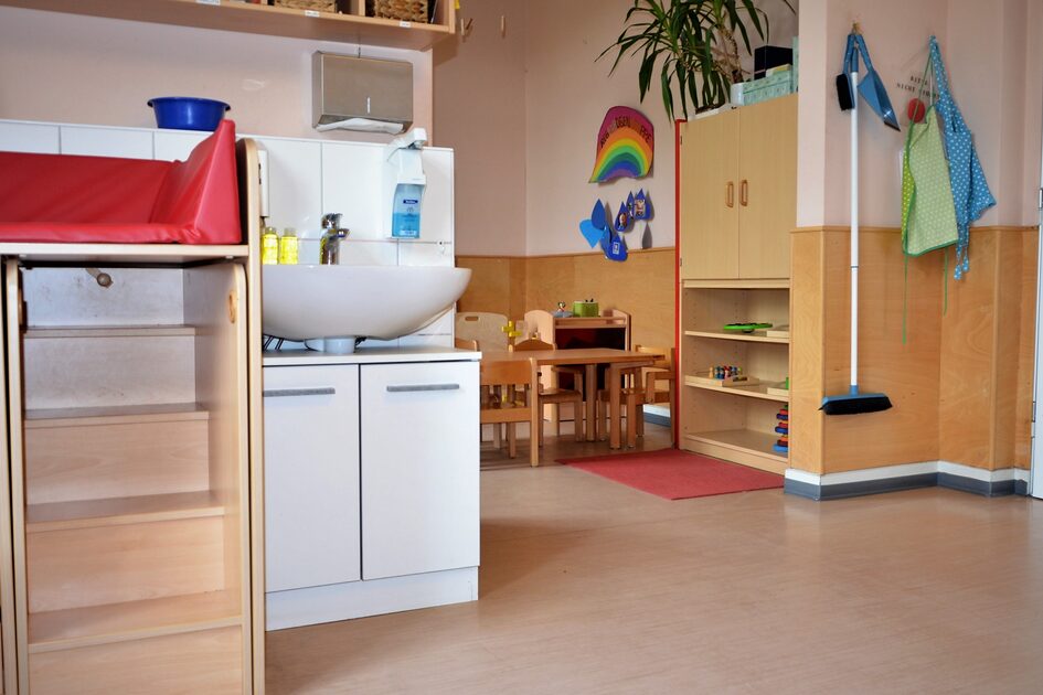 A view of a crèche group with a washbasin and a changing table. In the background is a table with several chairs