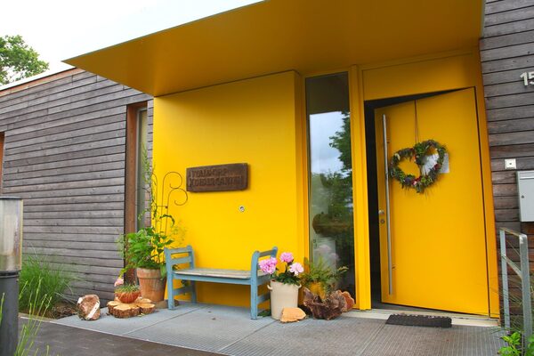 L'ingresso giallo dell'asilo nido con una panchina di legno verde, la targhetta e un cuore sulla porta