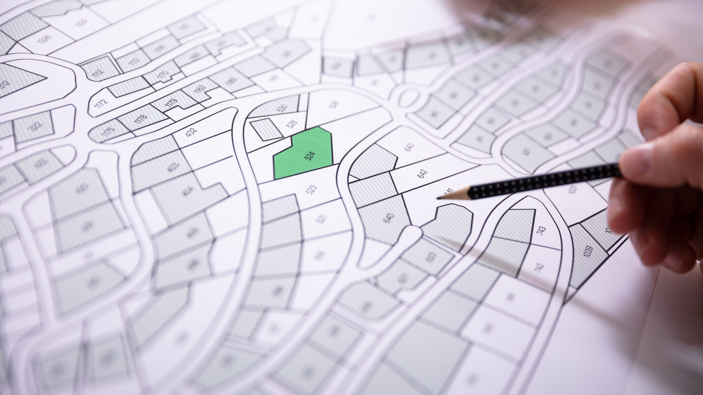 Nahmaufnahme einer Karte mit Grundstücken und einer Hand mit Bleichstift