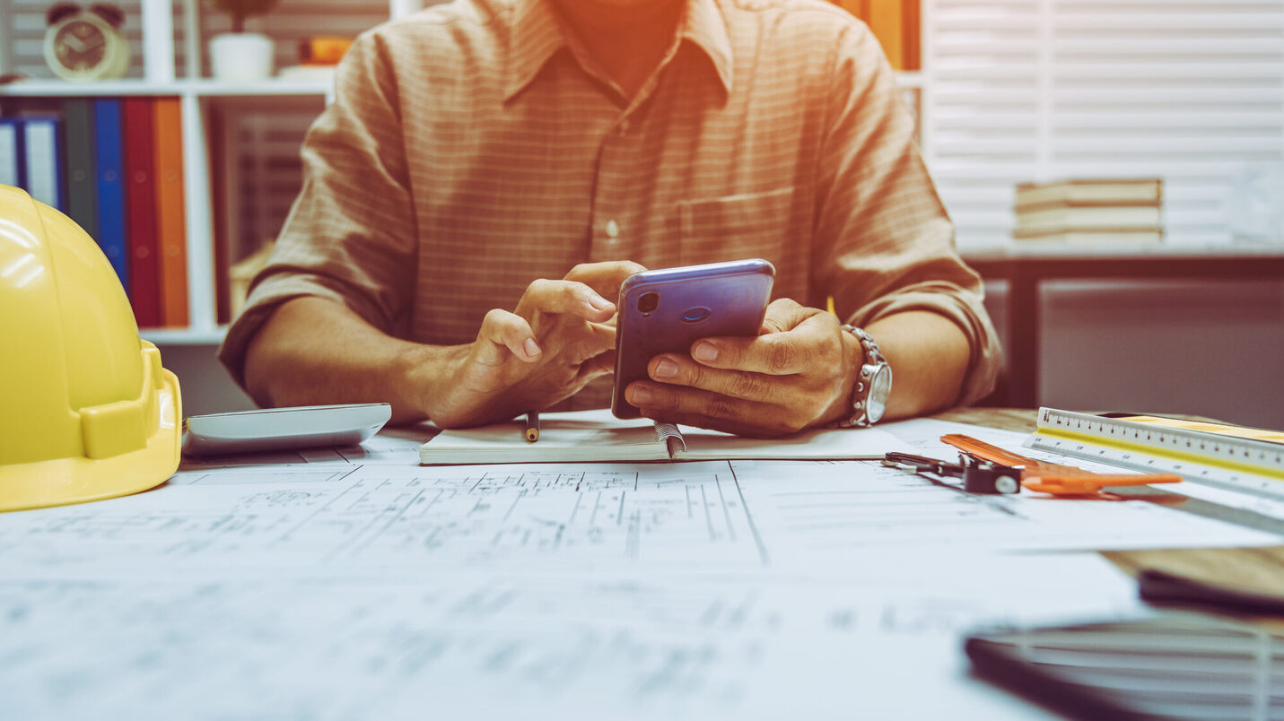Bauleiter sitzt am Schreitbisch und nutzt ein Handy