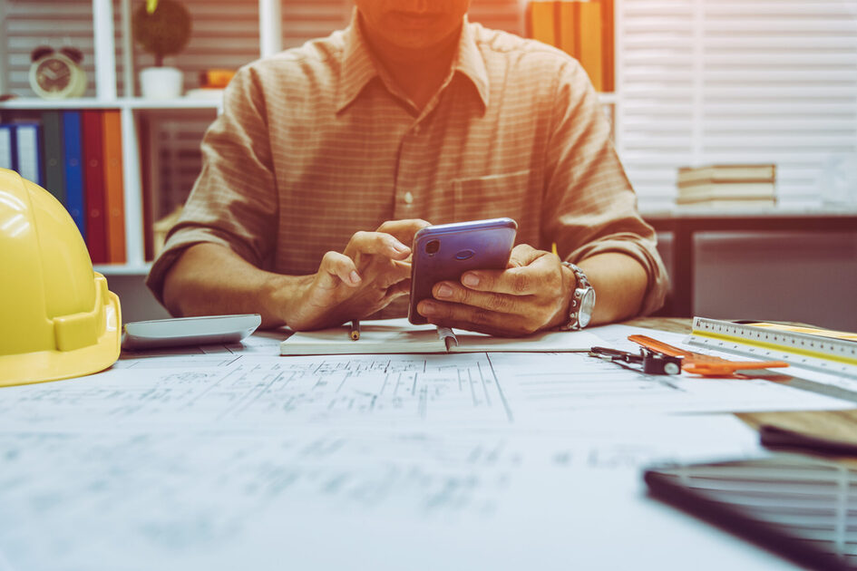 Bauleiter sitzt am Schreitbisch und nutzt ein Handy