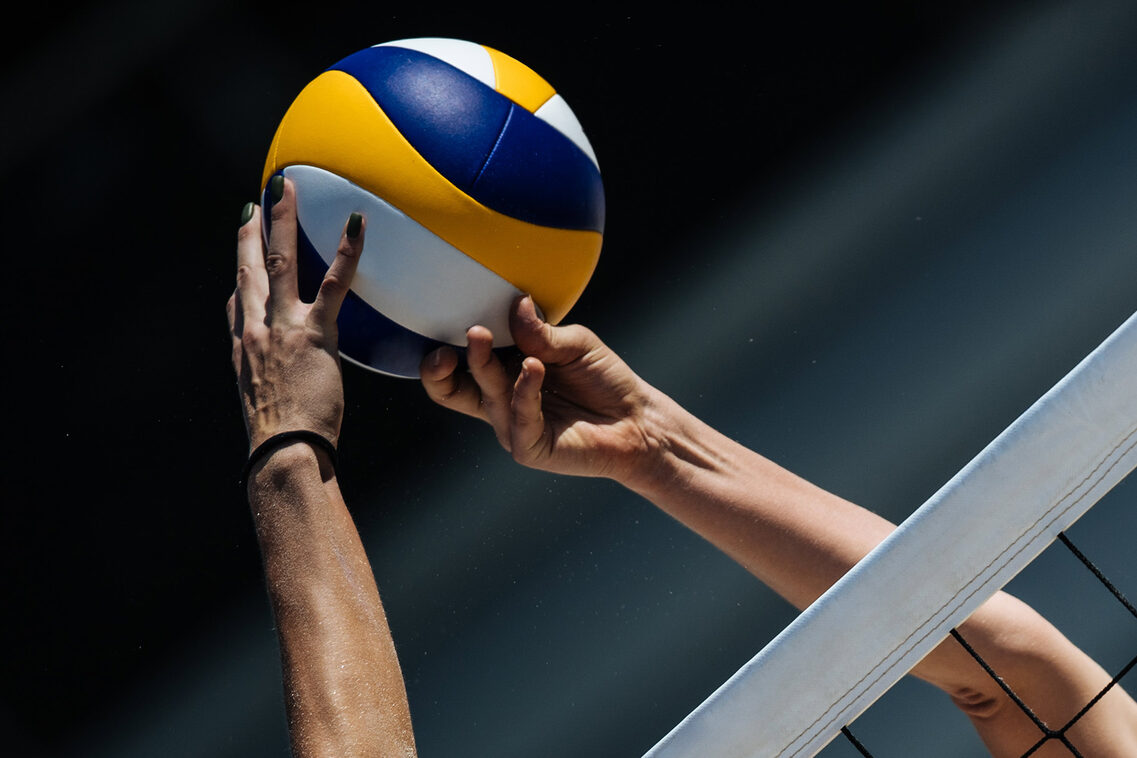 Frauenhände und -arme samt Voleyball und Volleyballnetz.