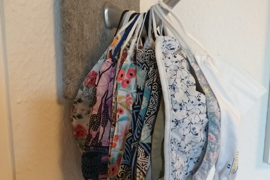 Viele genähte Stoffmasken hängen übereinander an einem Haken