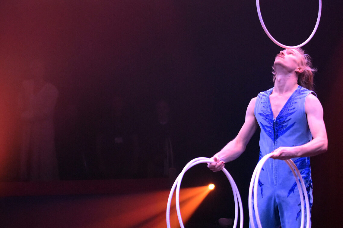 Artist Roni Heimo balanciert einen Ring auf der Stirn und hat jeweils zwei weitere in seinen Händen