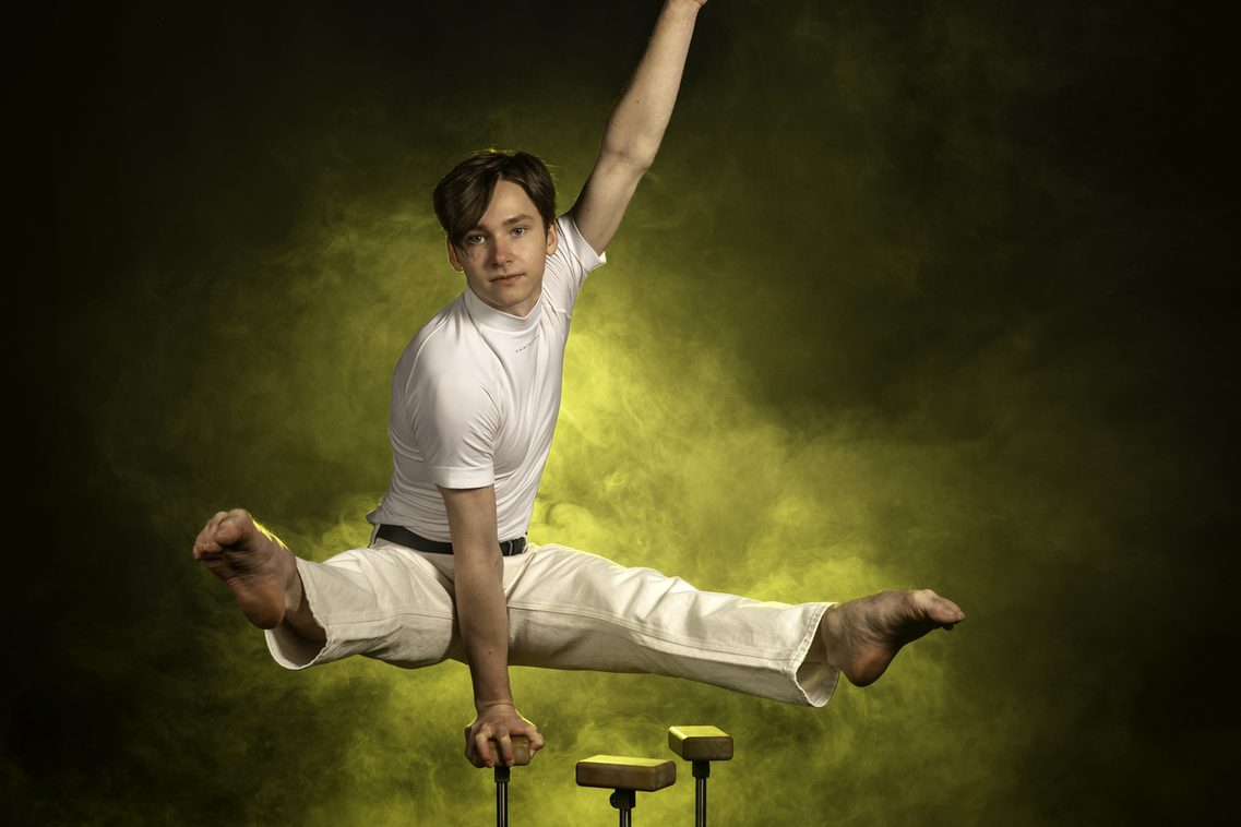 Ein junger Mann in einer beeindruckenden Position auf einem Arm mit beiden Füßen nach vorne im Spagat gestreckt – die Kunst der Equilibristik