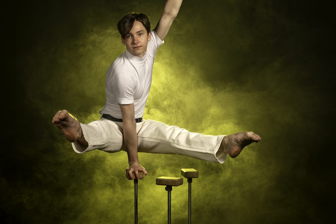 Ein junger Mann in einer beeindruckenden Position auf einem Arm mit beiden Füßen nach vorne im Spagat gestreckt – die Kunst der Equilibristik