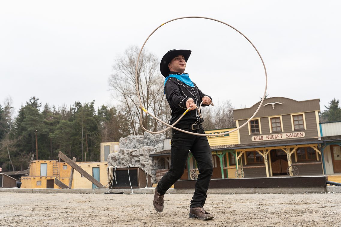 Ein Western-Künstler im authentischen Cowboy-Outfit schwingt meisterhaft sein Lasso, während er sich wie durch Zauberhand langsam in ein kreuzförmiges Monument verwandelt