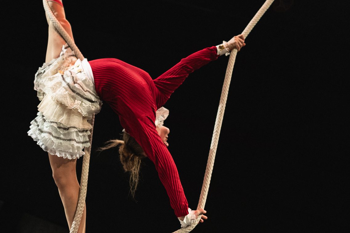 Eine Frau in vertikaler Spagat-Position zeigt am Seil eine Rückbeuge in der Luft – Kunst des Schwungseils & Clownerie
