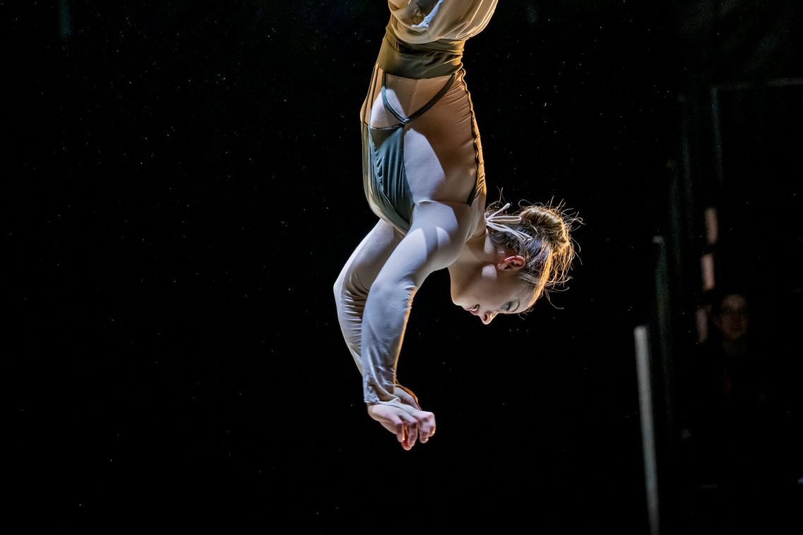 Eine Trapezartistin hängt in einer eleganten Pose mit dem Kopf nach unten.