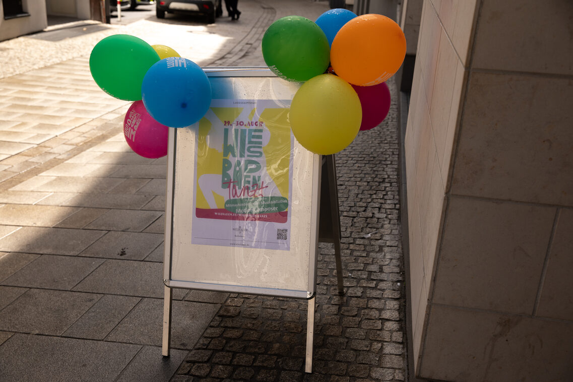 Plakat von Wiesbaden tanzt auf einem Plakatständer mit Luftballons