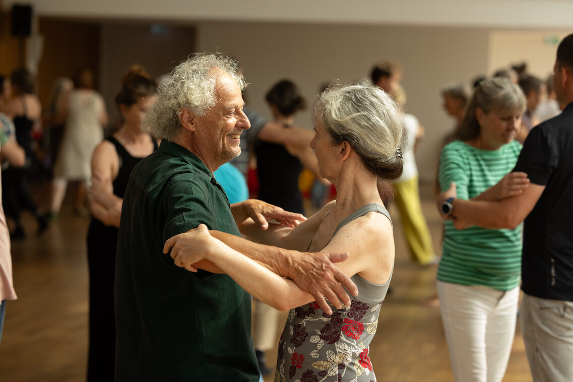 Ein älteres Paar tanzt und lächelt sich an.