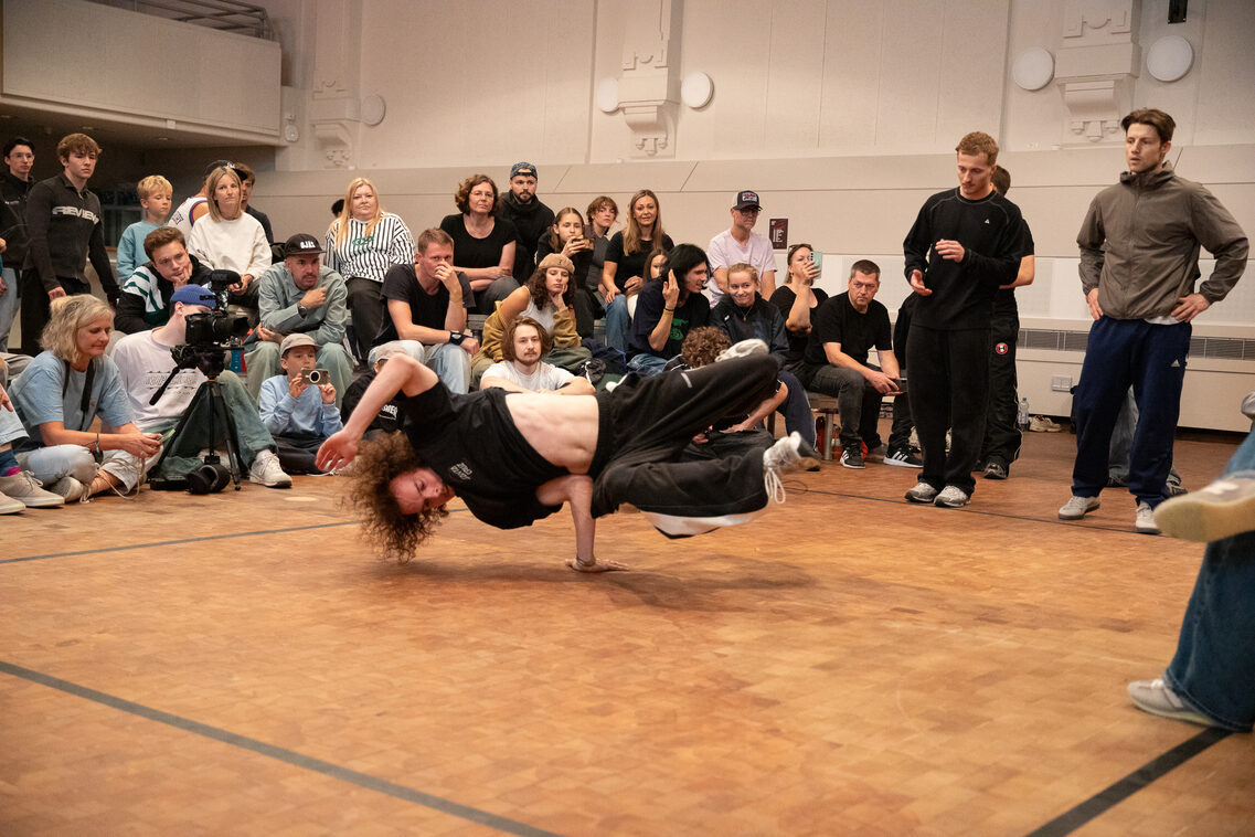 Eine Person stützt sich beim Breakdance auf den Unterarm und steht horizontal in der Luft.