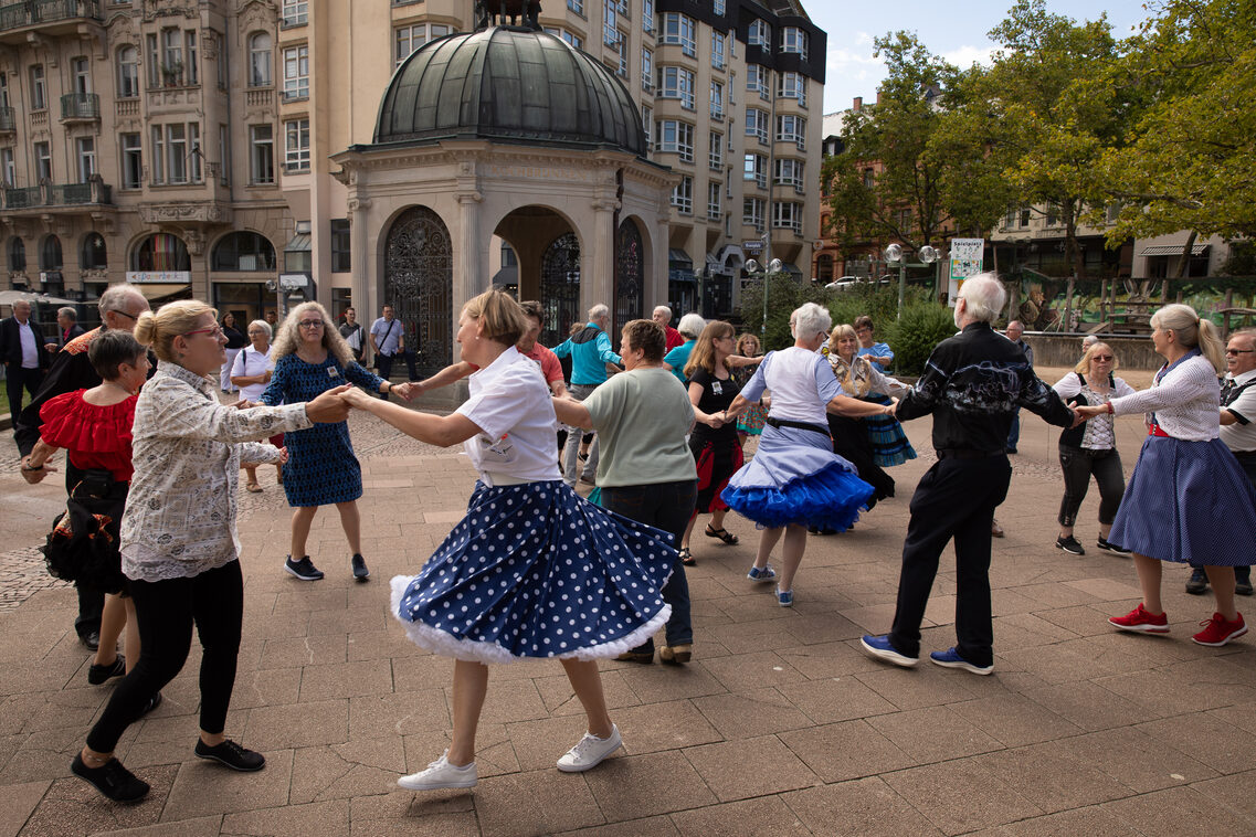 Menschen tanzen einen Kreistanz auf dem Kranzplatz. Die weiblichen Personen tragen zum Teil weite Röcke mit Petticoat.