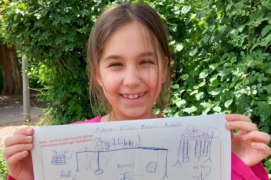 Ein junges Mädchen mit langen braunen Haaren steht draußen vor einer grünen Hecke und lächelt breit. Sie trägt ein pinkfarbenes Oberteil. In ihren Händen hält sie eine Zeichnung ihres Wunsch-Spielplatzes, die mit blauen und schwarzen Stiften erstellt wurde. Darauf sind ein Kletterturm, eine Seilbahn, ein Karussell und ein Pool zu sehen. Ihr Name „Kübra“ steht in großen Buchstaben über der Zeichnung. Auch hier sind die Logos von GWW und der Stadt Wiesbaden zu erkennen.