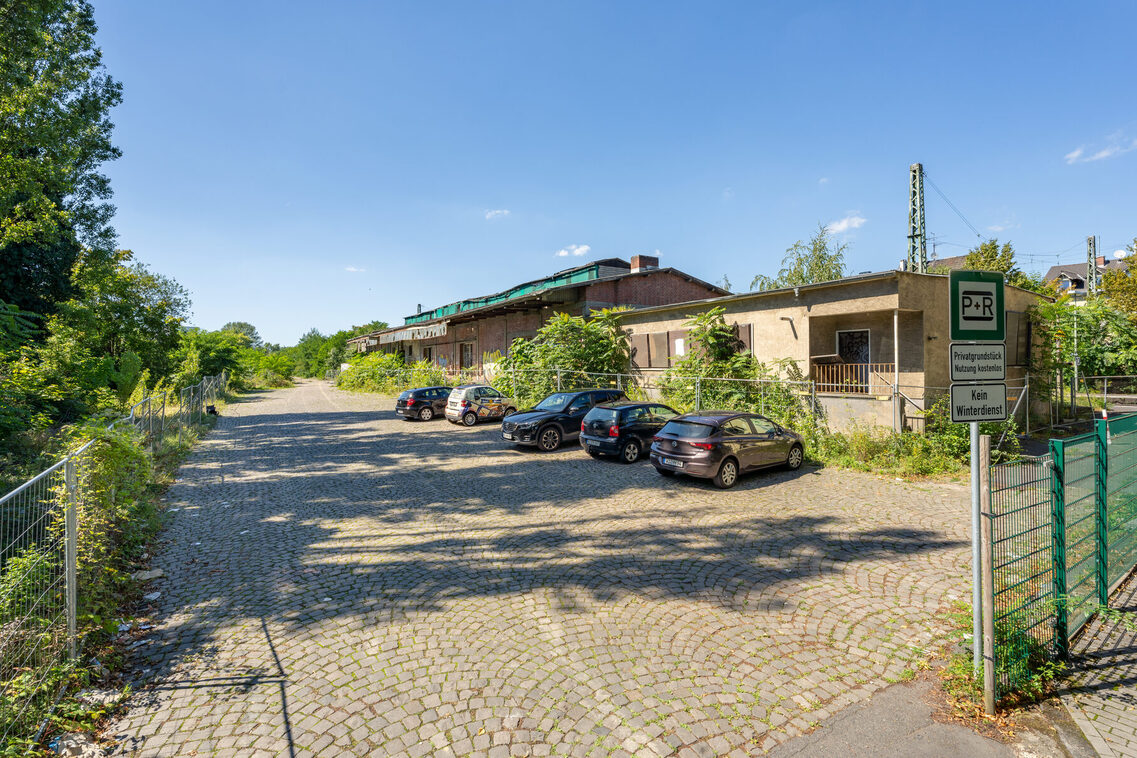 Autos parken vor der verfallenen Güterhalle.