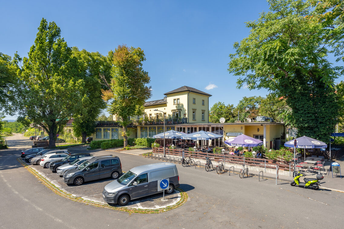 Der heutige Regionalbahnhof Wiesbaden-Biebrich mit Außengastronomie und Bahnhofsvorplatz. Autos und asphaltierte Flächen prägen den öffentlichen Raum.